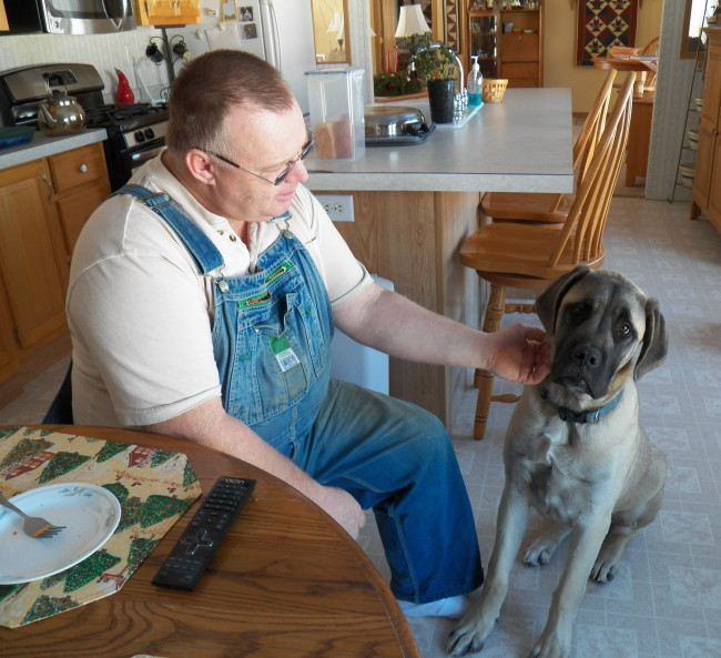 A man wearing overalls petting a dog