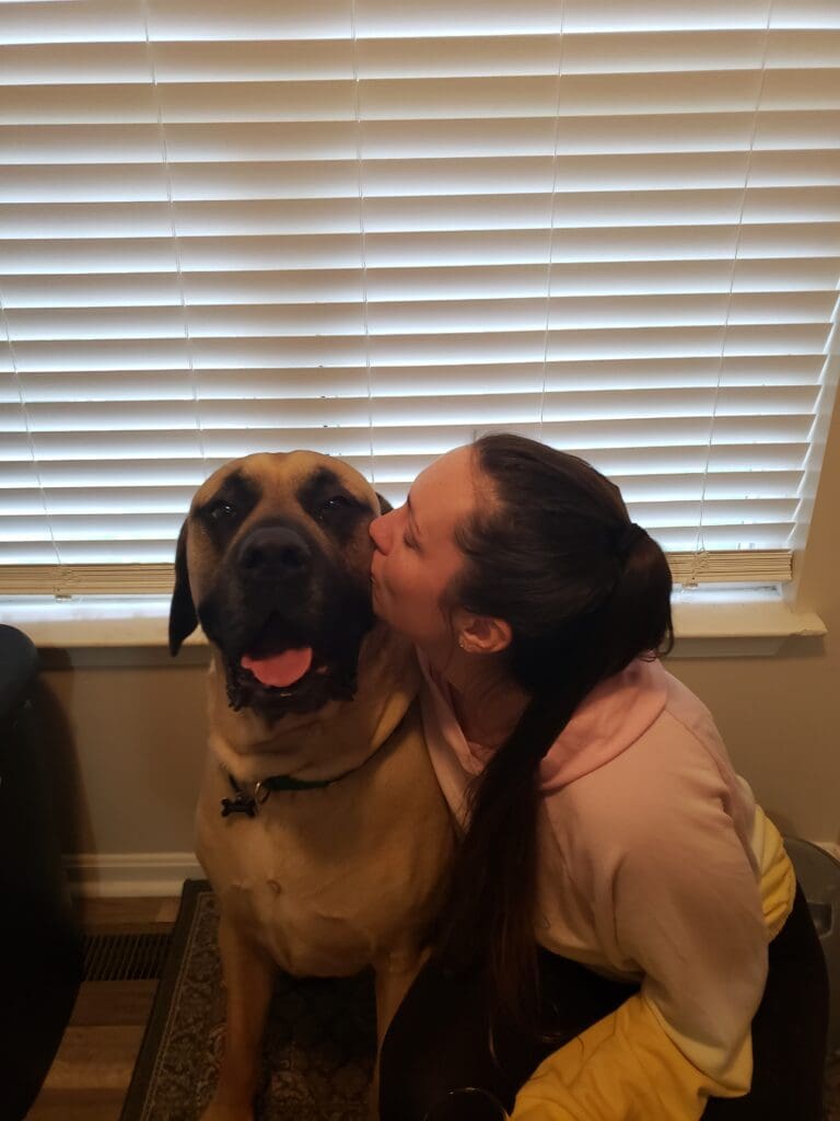 A woman kissing her dog in front of the window.
