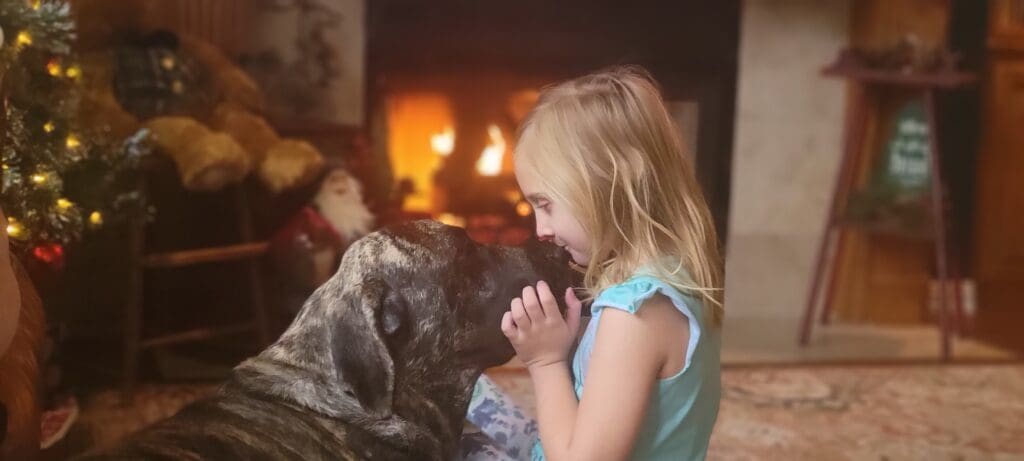 A little girl is petting a dog in front of the fireplace.