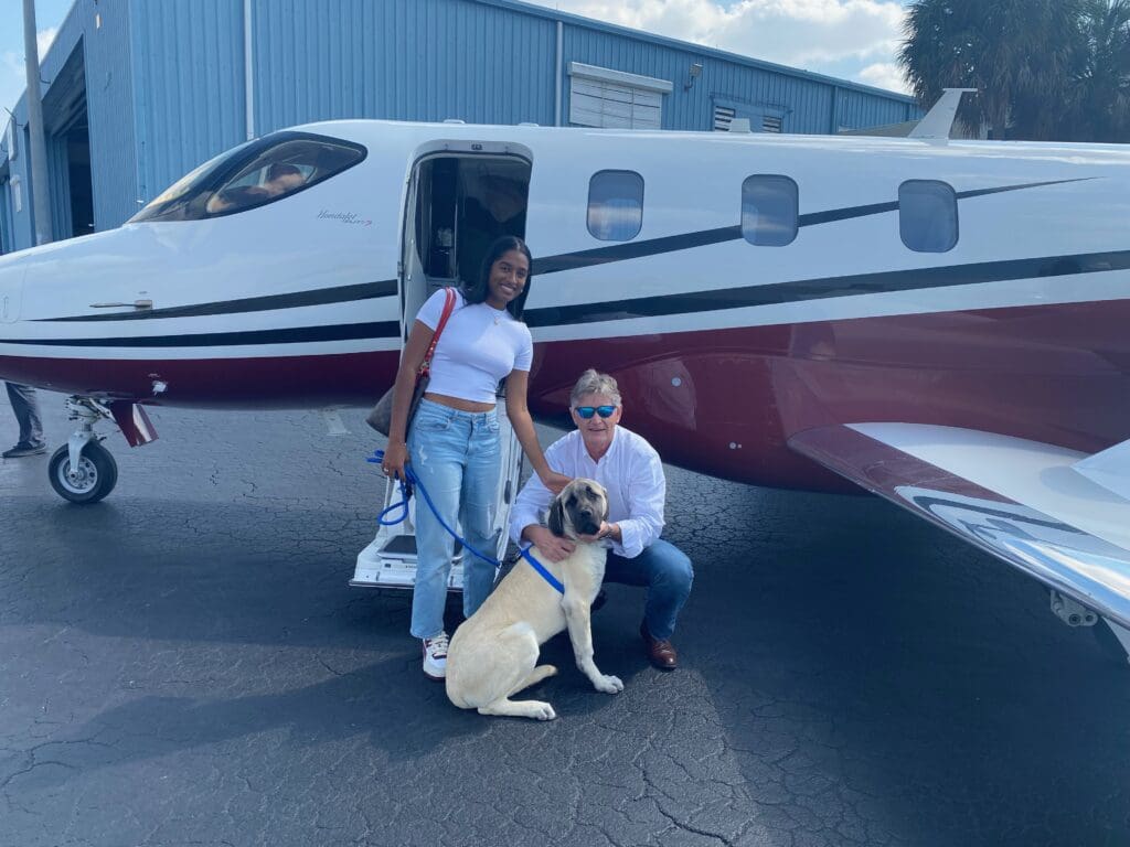 A man and woman with their dog standing in front of an airplane.